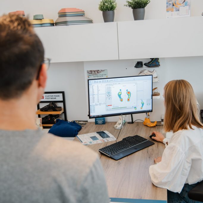Podoloog bespreekt resultaten van een statische en dynamische drukmeetanalyse / voetanalyse op computerscherm met patiënt.